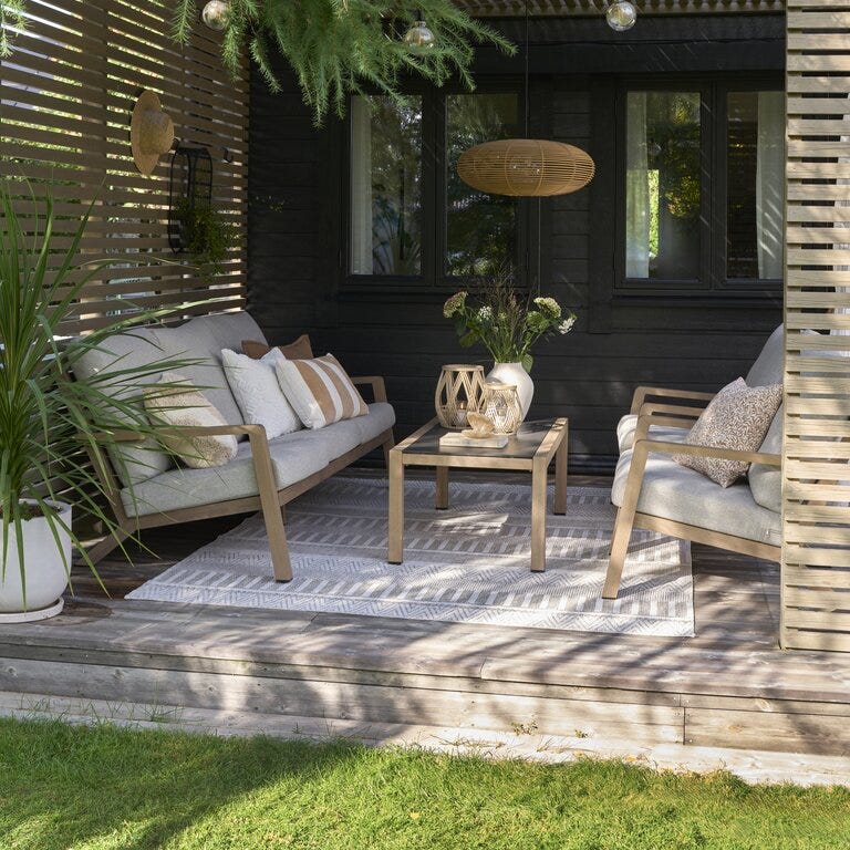 Sofagruppe med grå puter og lys ramme under pergola ute ved husveggen