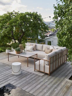 Beige hjørnesofa med treramme på terrasse i en grønn hage