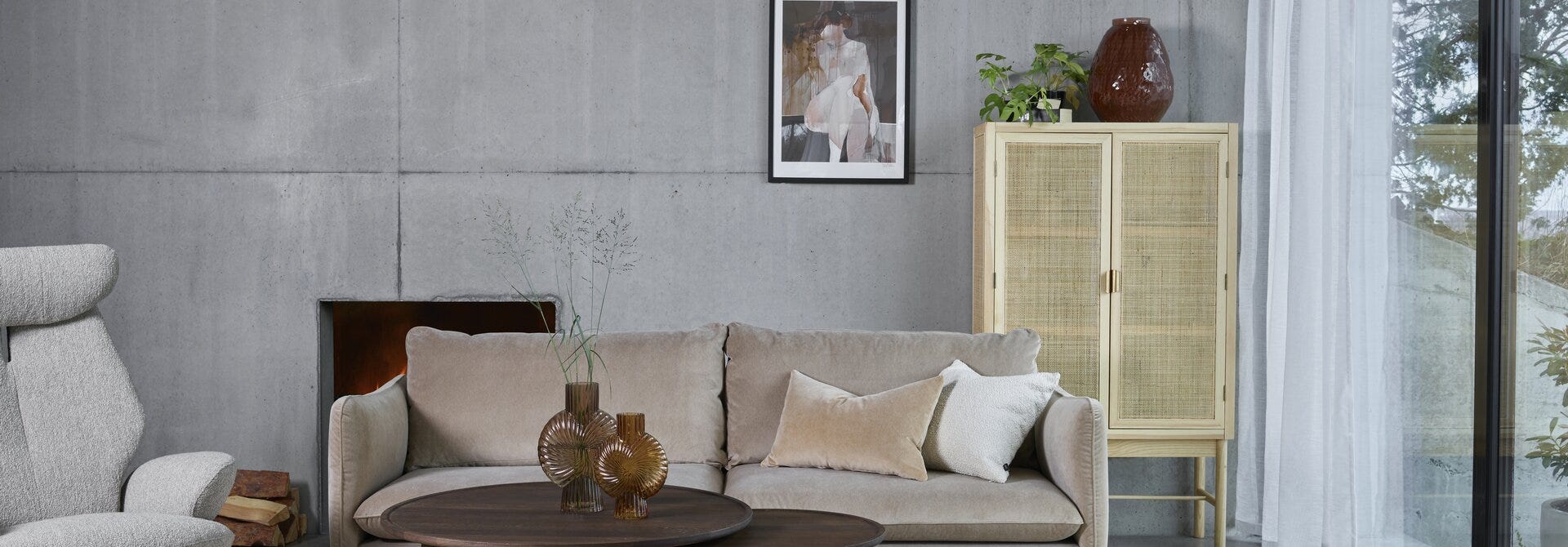Rottingskap mot betongvegg i nordisk stue med beige velursofa Rottingskap mot betongvegg i nordisk stue med beige velursofa