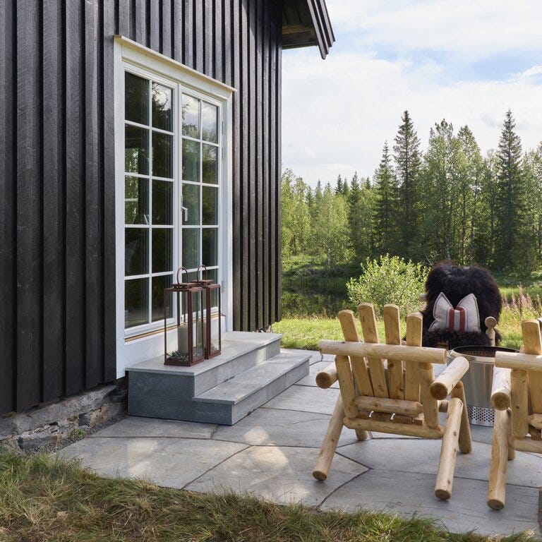 Uteplass med trestoler og lykt ved sort hytte – Eventyrlig oppussing Snåsa