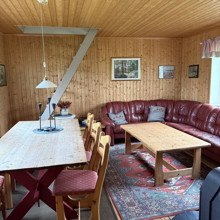 Før-bilde fra stueområdet i Eventyrlig oppussing Snåsa – rødt hjørnesofasett, spisebord og trepanel på vegger og tak.