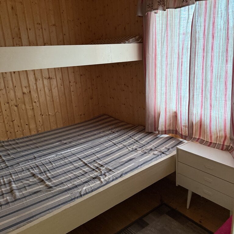 Før-bilde fra Eventyrlig oppussing Snåsa – enkel sovealkove med køyeseng, panelvegger og rutete gardiner.