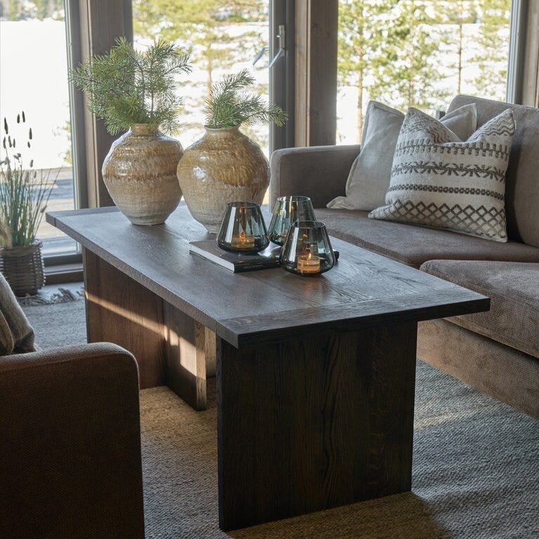Stuebord i mørkt tre med dekorvaser og telysholdere foran sofa med puter etter oppussing i Setesdal